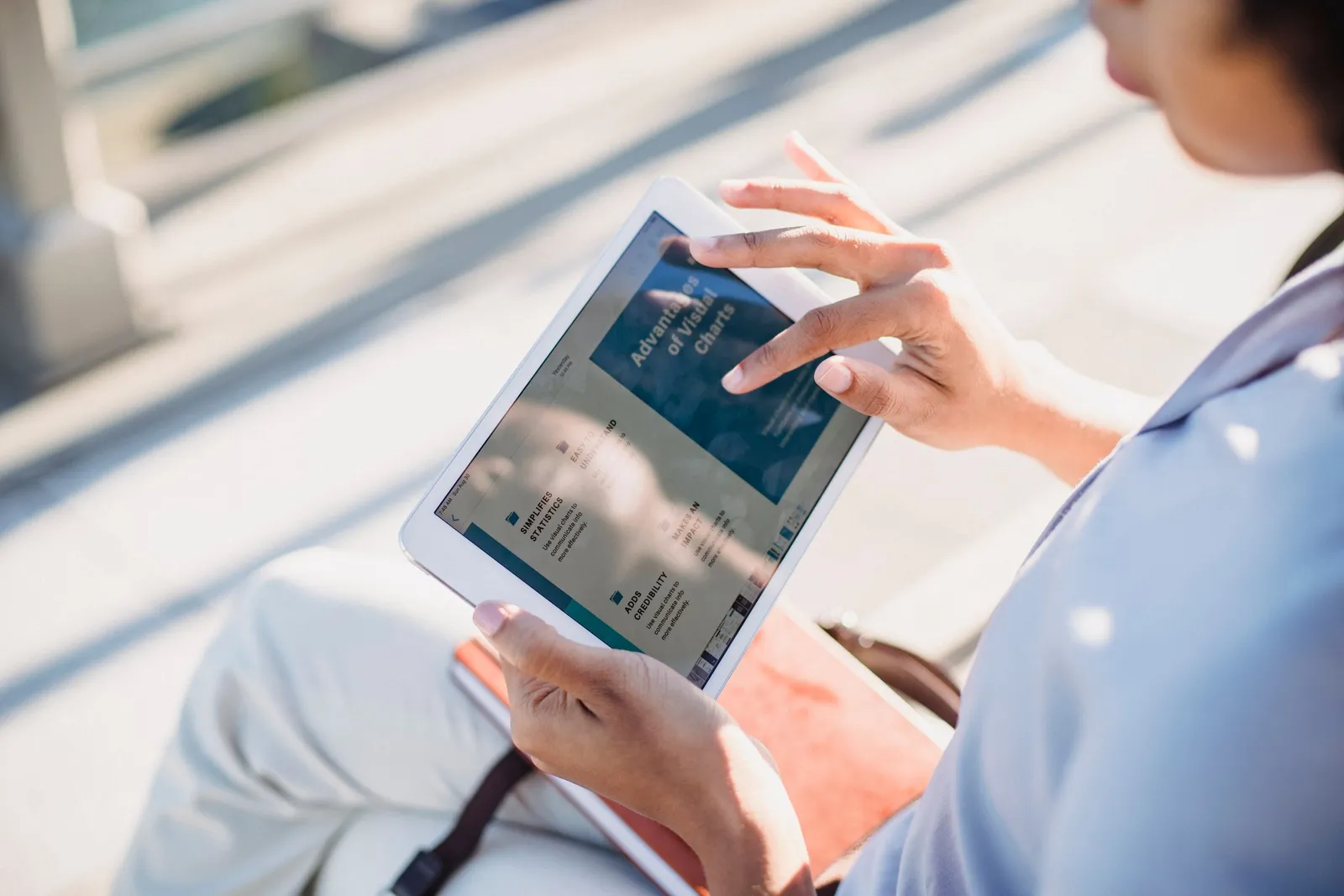 A person reads an article on a tablet outdoors in bright sunlight.