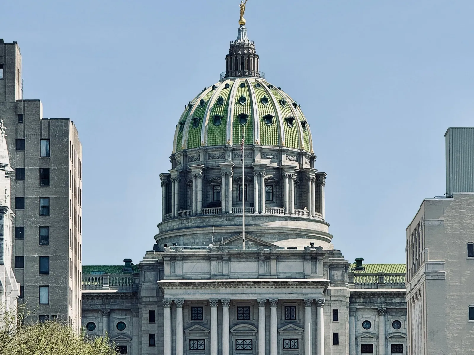 The green-tiled dome of the Pennsylvania State Capitol in Harrisburg rises above its front steps on a clear spring day.