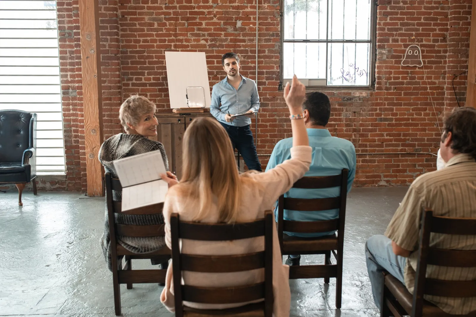 A volunteer raises her hand during a small training session in a brick-walled room.